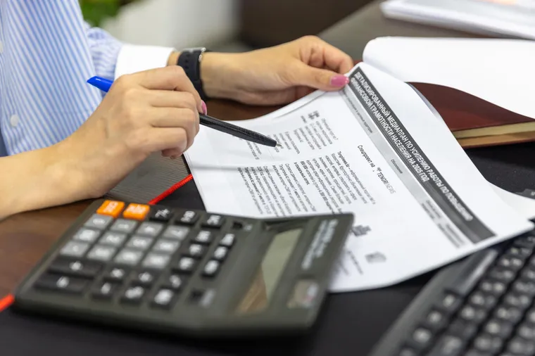 A finance professional reviewing printed documents with a calculator at a desk